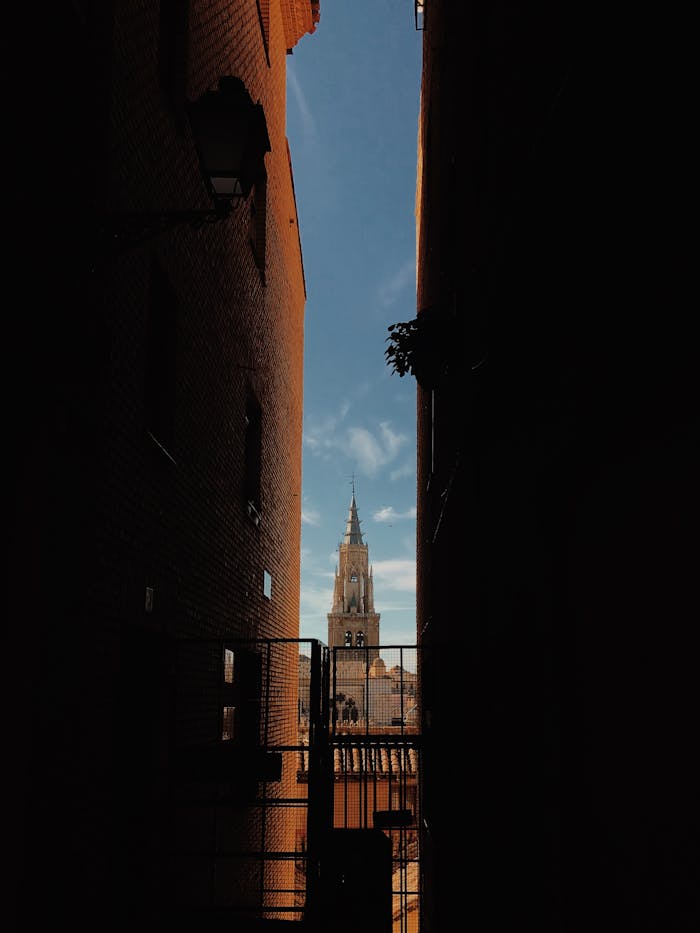 Dynamic view of Toledo's Gothic cathedral spire framed by traditional alley architecture.