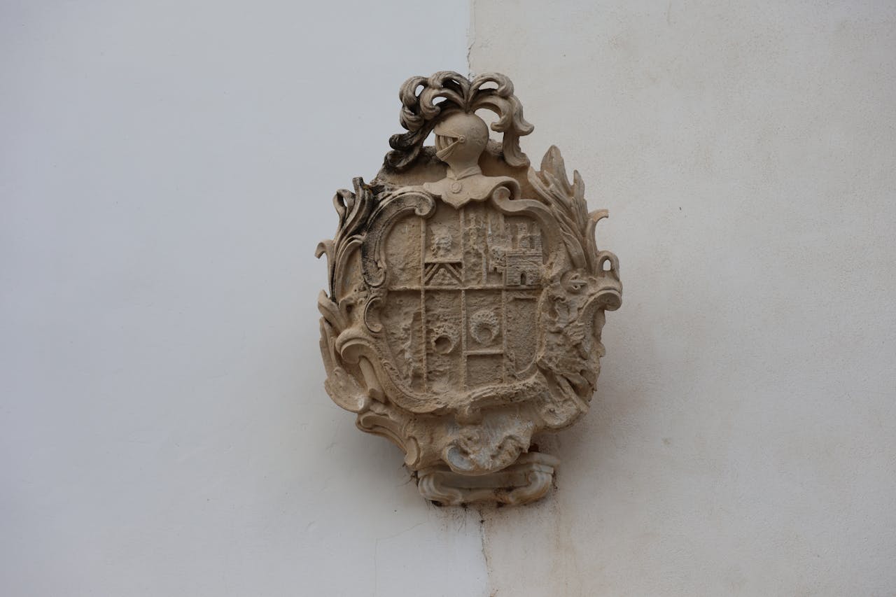 Detailed stone heraldry plaque featuring intricate designs on a white wall in Puerto Real, Andalucía, Spain.